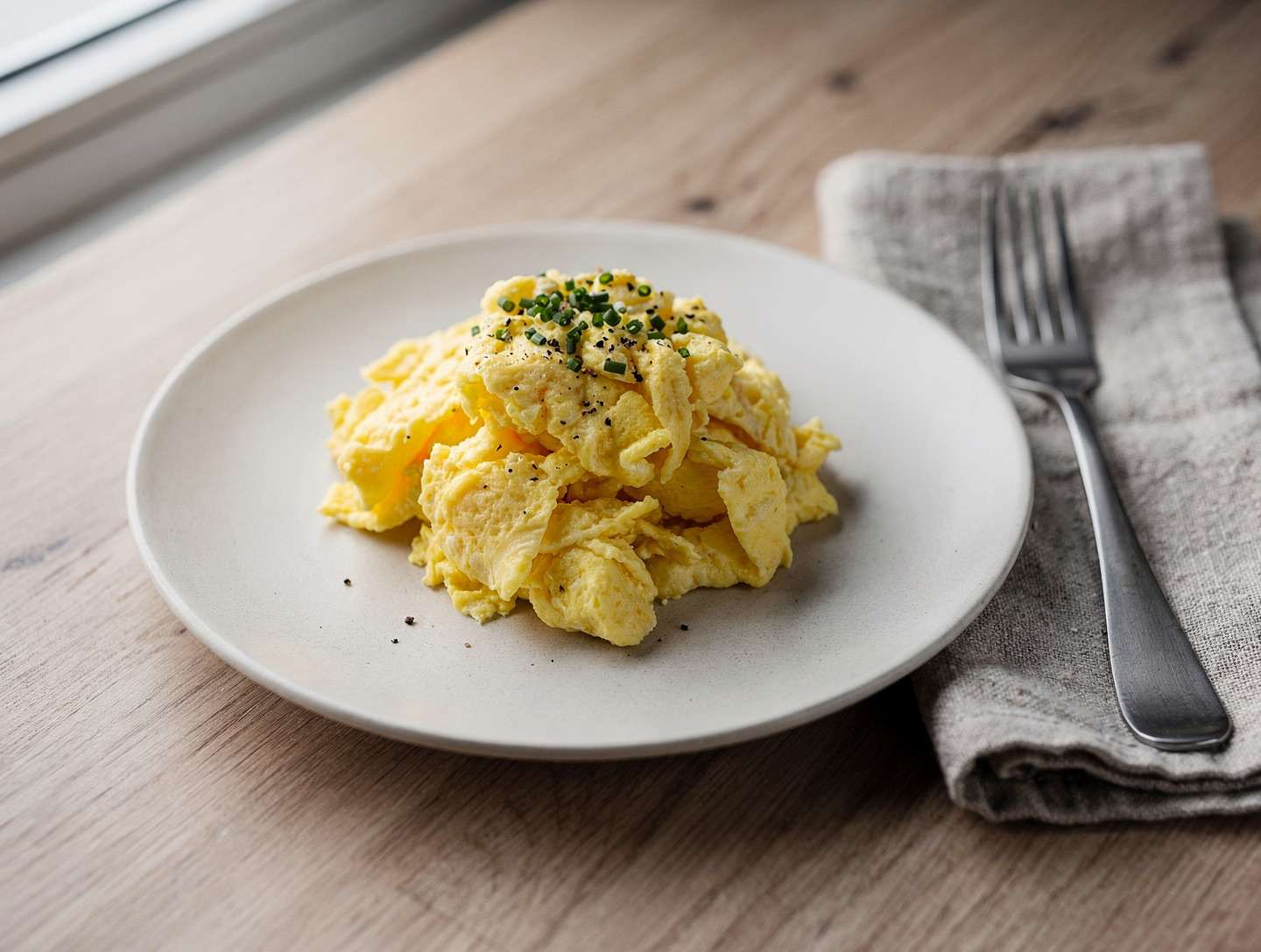 Krämig äggröra med gräslök och svartpeppar på en off-white tallrik